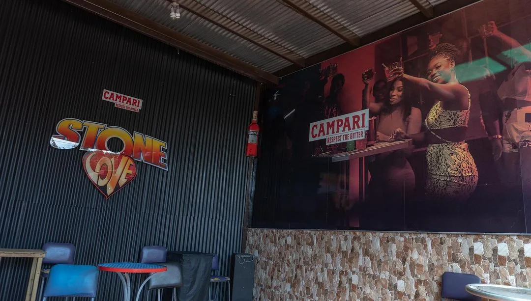 Stone Love wall sign and large Campari mural above tables and chairs inside a bar